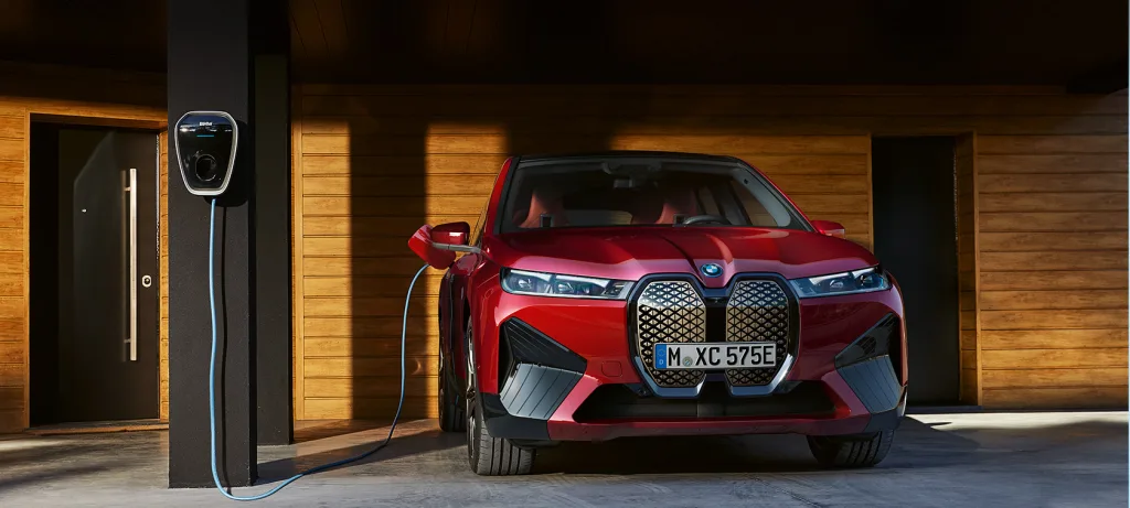 BMW iX rouge en charge sur une wallbox BMW murale, dans le garage d'une maison